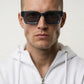Man wearing dark sunglasses and a white hoodie against a light background