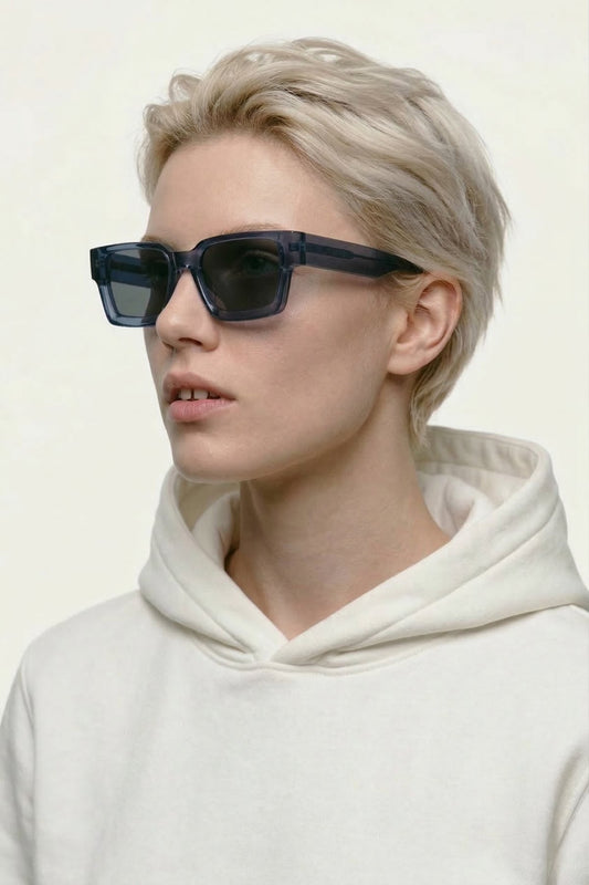 Person wearing dark sunglasses and a white hoodie against a light background