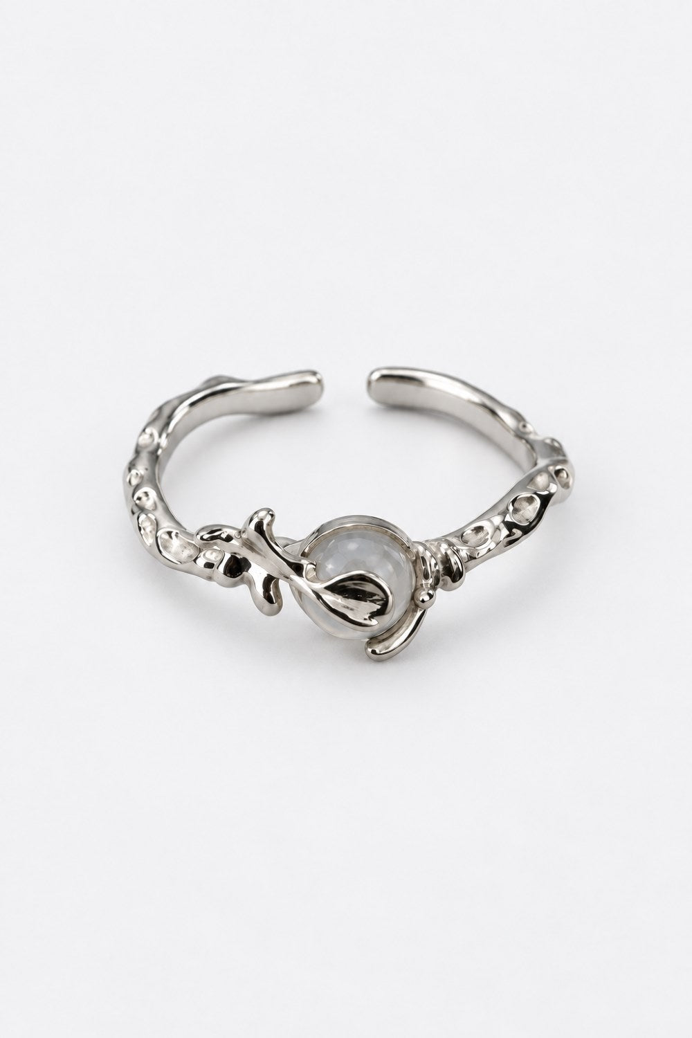 A silver-toned open ring cuff featuring a central teardrop-shaped setting with a milky white stone and textured, organic detailing along the band, shown on a plain white background.