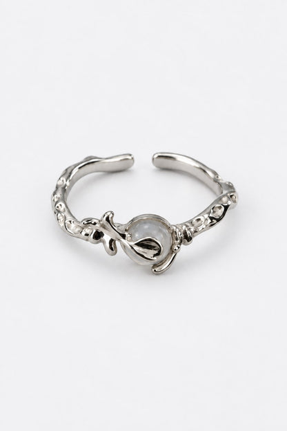 A silver-toned open ring cuff featuring a central teardrop-shaped setting with a milky white stone and textured, organic detailing along the band, shown on a plain white background.