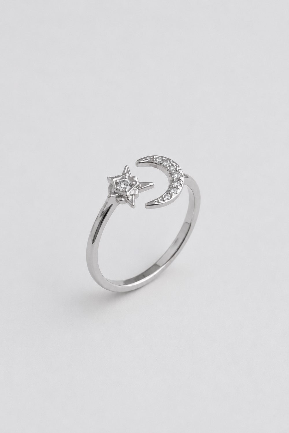 A silver-toned ring featuring a crescent moon and star design, accented with small clear stones, set against a plain light gray background.