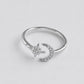 A silver-toned ring featuring a crescent moon and star design, both adorned with small clear stones, set against a plain light gray background.