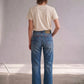 A model viewed from behind wearing blue cropped jeans, a cream t-shirt, and black high-heeled sandals in a minimalist studio setting.