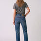 A woman viewed from behind wearing blue denim jeans, a dark gray t-shirt, and black high heels against a light gray studio background.