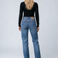 A woman viewed from behind wearing blue straight-leg jeans, a black long-sleeve top, and black heeled boots against a light gray studio background.