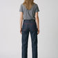 A woman viewed from the back wearing dark blue straight-leg denim jeans with red contrast stitching, a heather gray t-shirt, and black heels, against a light gray studio background.